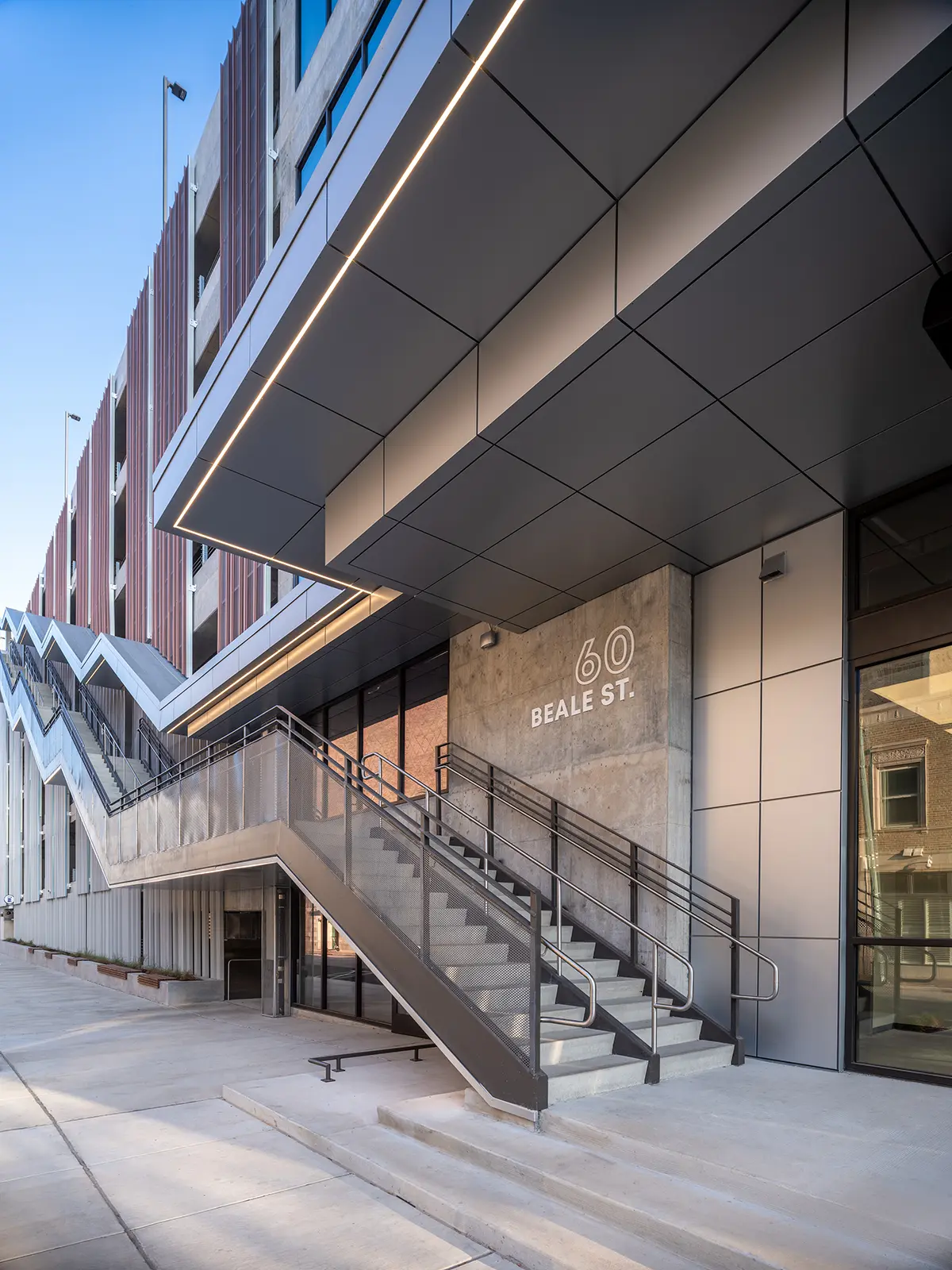 Modern building facade at 60 Beale St., features geometric design, large overhang, stairs, and glass windows, evoking a sleek, urban feel.
