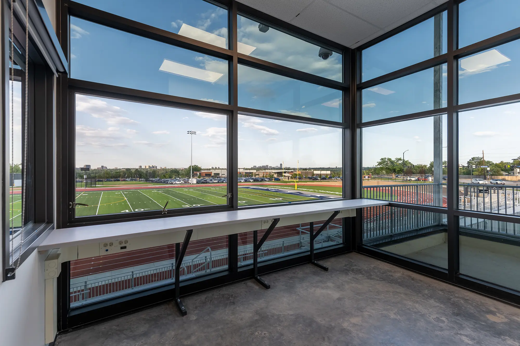 Spacious room with large glass windows overlooking a sunlit football field and running track, conveying a sense of openness and tranquility.