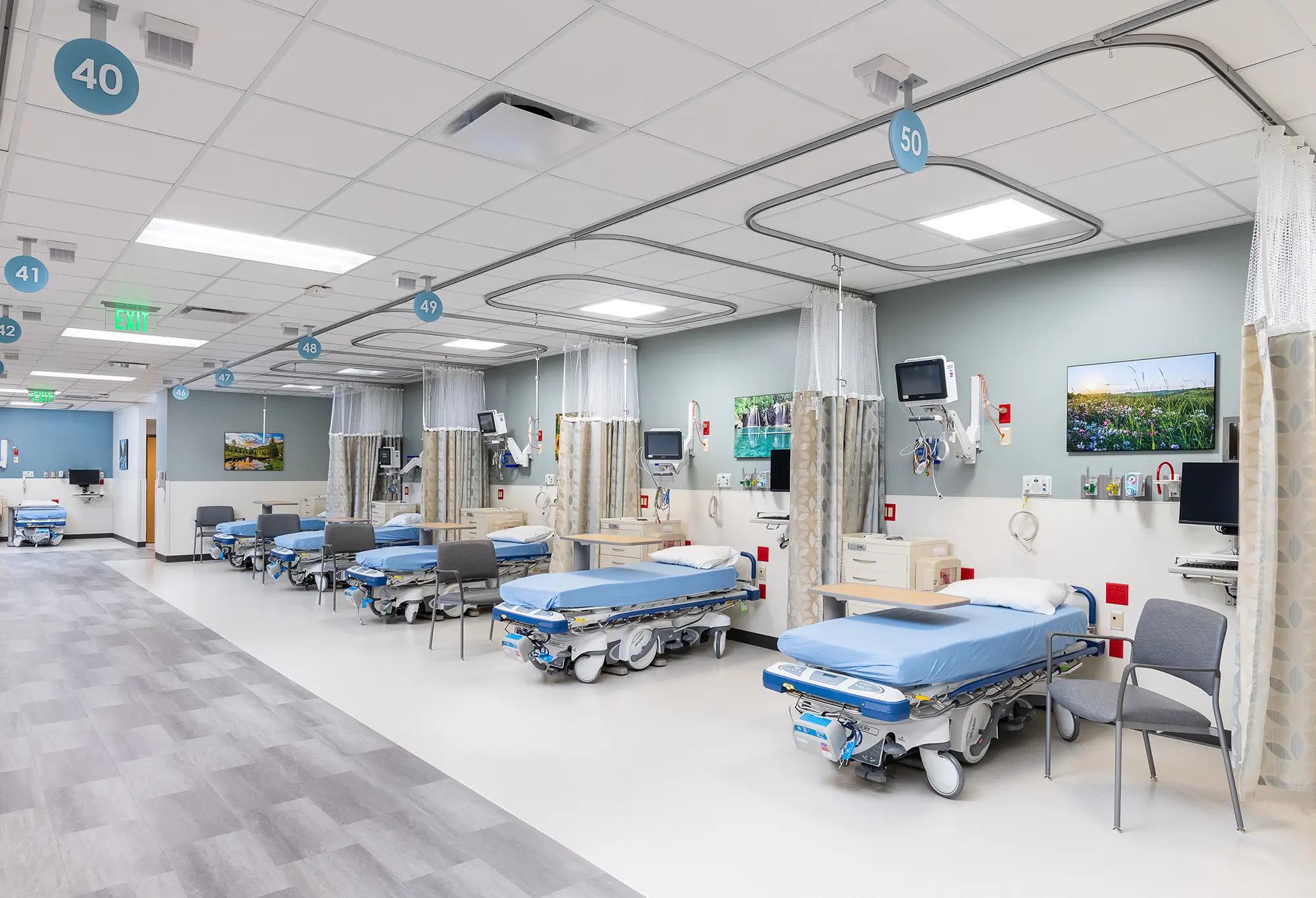 A hospital ward with multiple empty beds, each separated by curtains. Medical equipment and monitors are beside each bed, creating a clean, organized environment.
