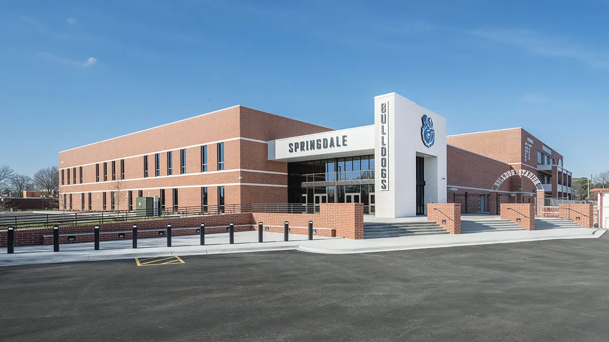Modern brick school building with "Springdale Bulldogs" sign and large windows, under a clear blue sky. The scene is bright and inviting.