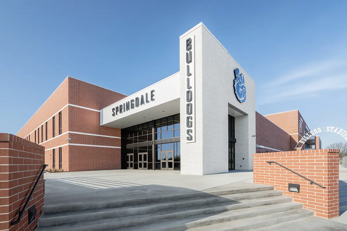 Wide view of a modern school building with "Springdale Bulldogs" signage. Red brick exterior, white facade, blue logo; entrance feels welcoming.