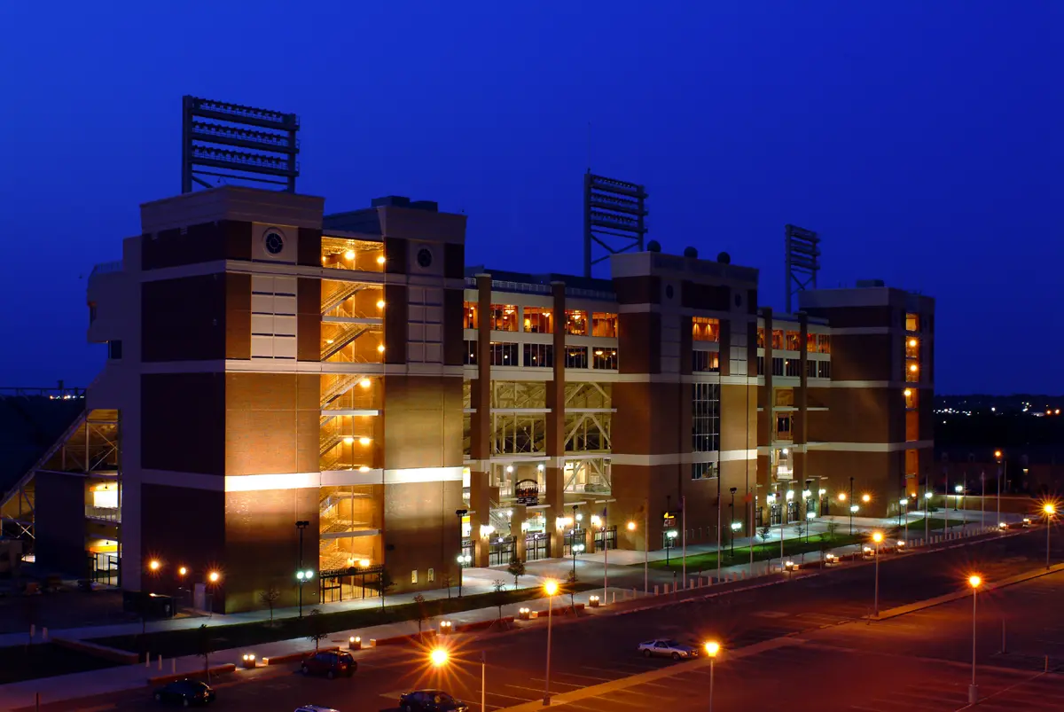 Illuminated stadium at night, showcasing brick facade and bright lights against a deep blue sky. The warm glow creates a welcoming, vibrant atmosphere.