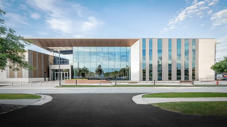 Modern building with large glass windows and vertical panels, set against a blue sky. The minimalistic design and open space evoke a calm, inviting atmosphere.