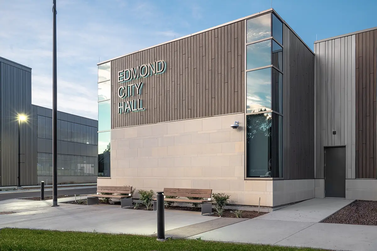 Modern Edmond City Hall building with a wood-clad design, large windows, and benches at the entrance. The atmosphere is calm and well-lit.