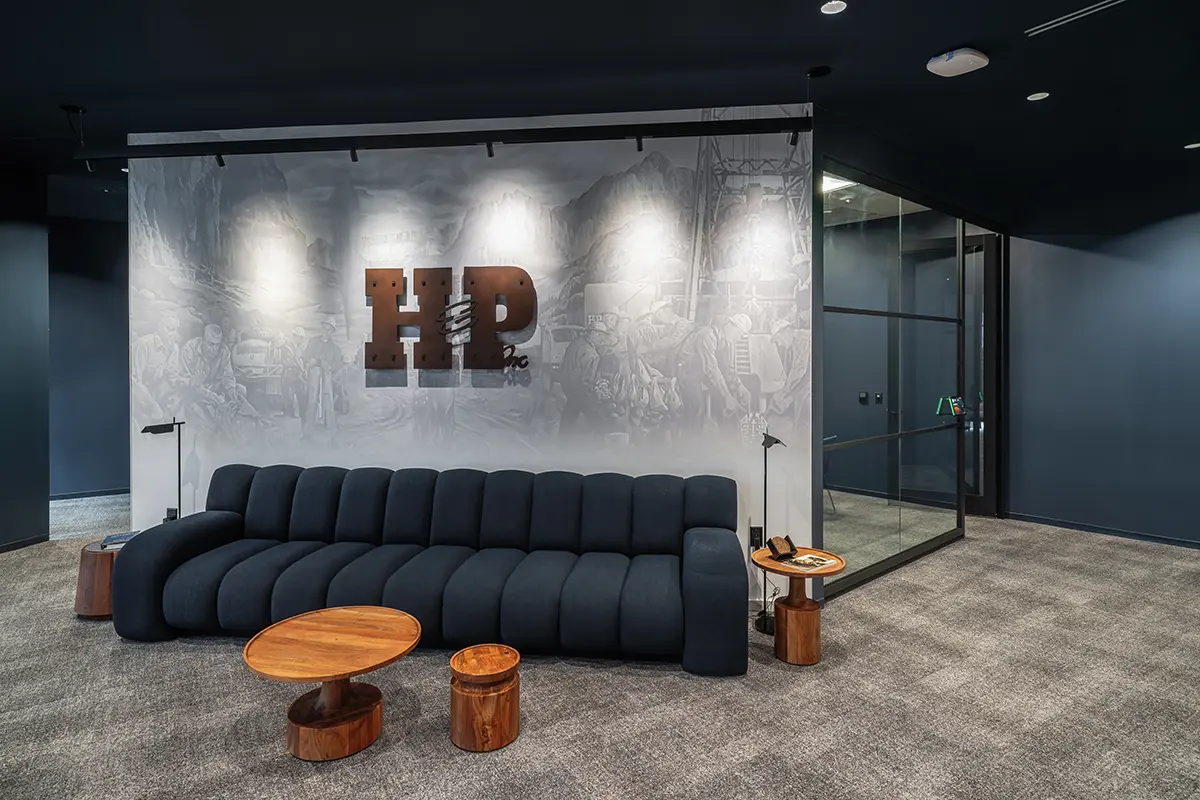 Modern office lobby with a dark, plush sofa and round wooden tables on gray carpet. “HP” logo on a backlit mural wall conveys a sleek, professional ambiance.