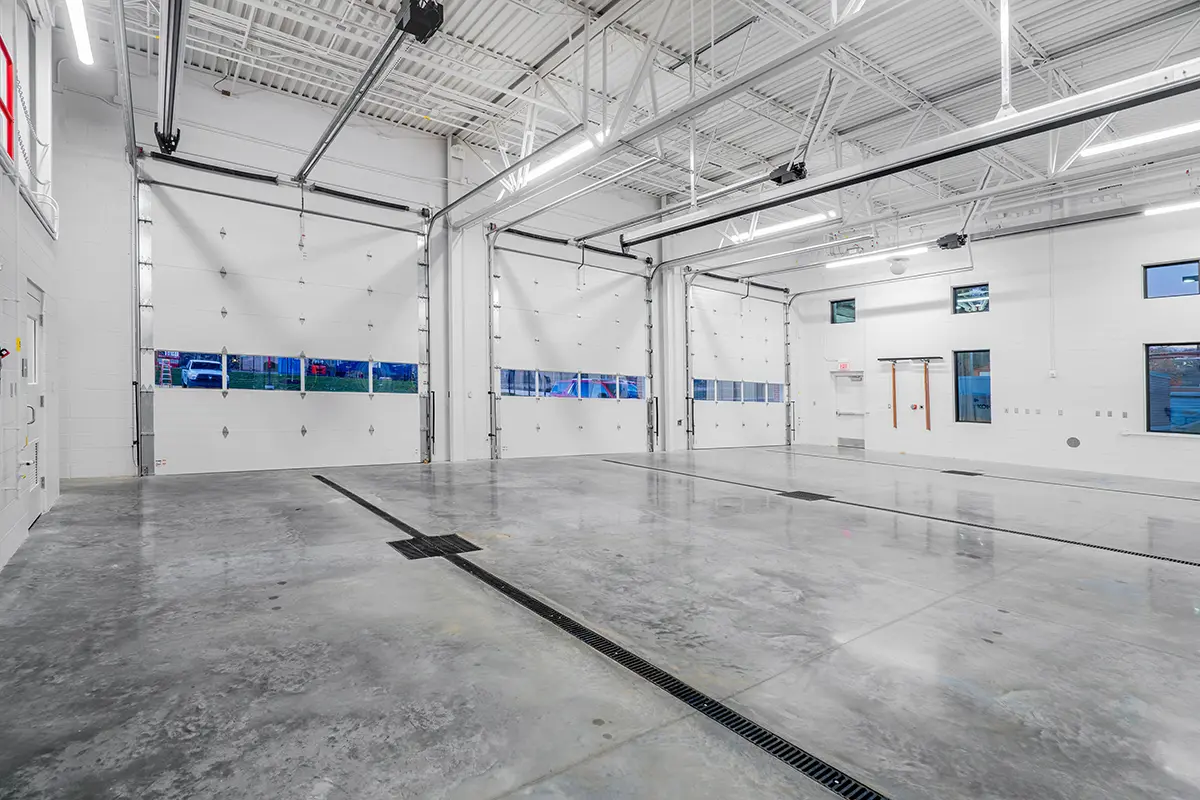 Spacious, clean, and bright industrial garage with polished concrete floors, white walls, and large overhead doors. High ceiling with exposed beams.