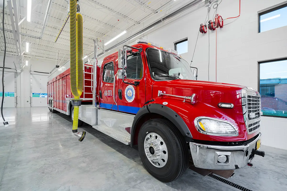 A vibrant red fire truck with chrome details is parked in a spacious, well-lit garage. The atmosphere is clean and orderly, conveying readiness.
