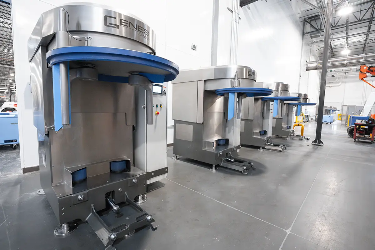 Modern industrial kitchen with three stainless steel dough mixers in a spacious, clean facility. High ceilings and bright lighting convey efficiency.