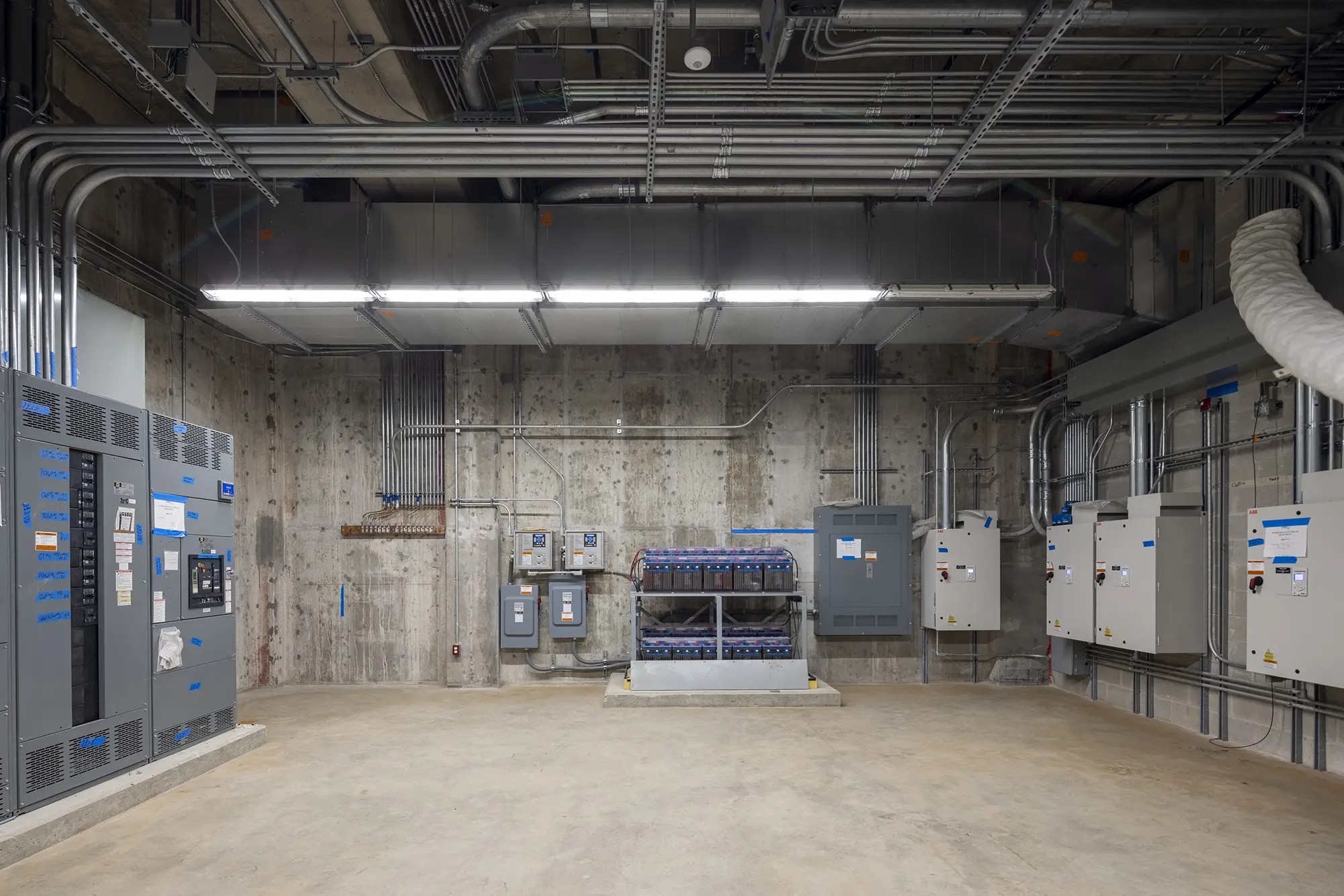 Industrial room with concrete walls and exposed pipes. Electrical panels and machinery line the walls. The atmosphere is sterile and utilitarian.