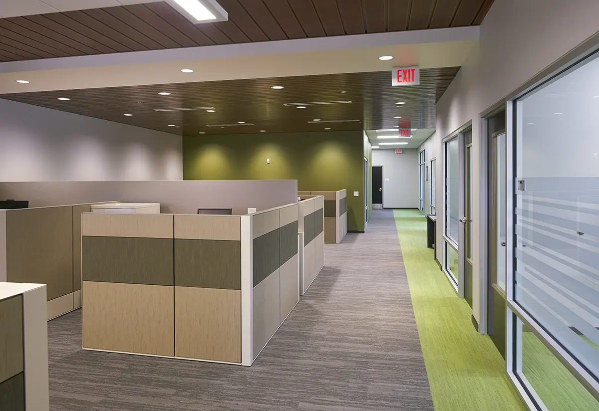 Modern conference room with a U-shaped wooden table, black swivel chairs, large windows revealing a scenic mountain view. Warm lighting and stone wall accentuate the space.