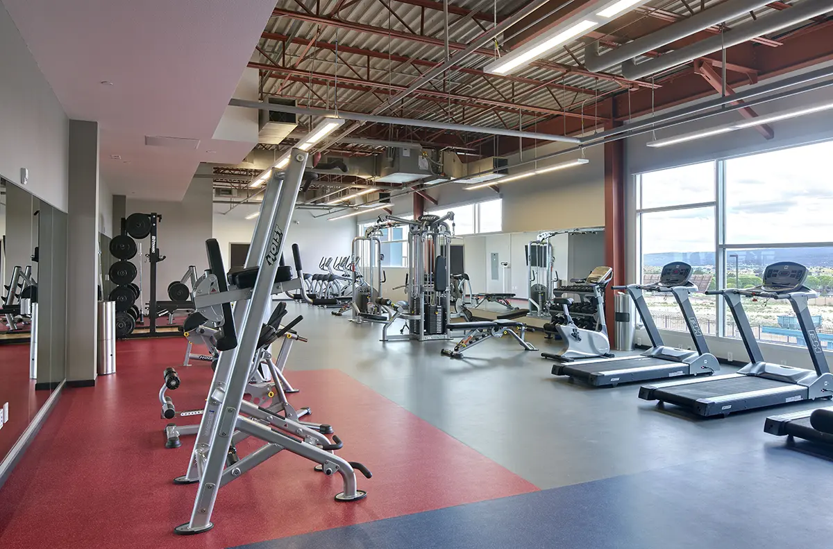 Modern office interior featuring a row of cubicles with beige and green panels, green accents, and an exit sign on the ceiling. Clean and professional ambiance.