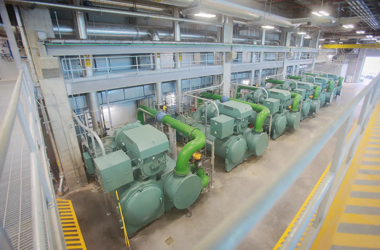 Industrial setting with large machinery in neat rows. Green pipes and equipment dominate the scene, conveying a sense of precision and order.