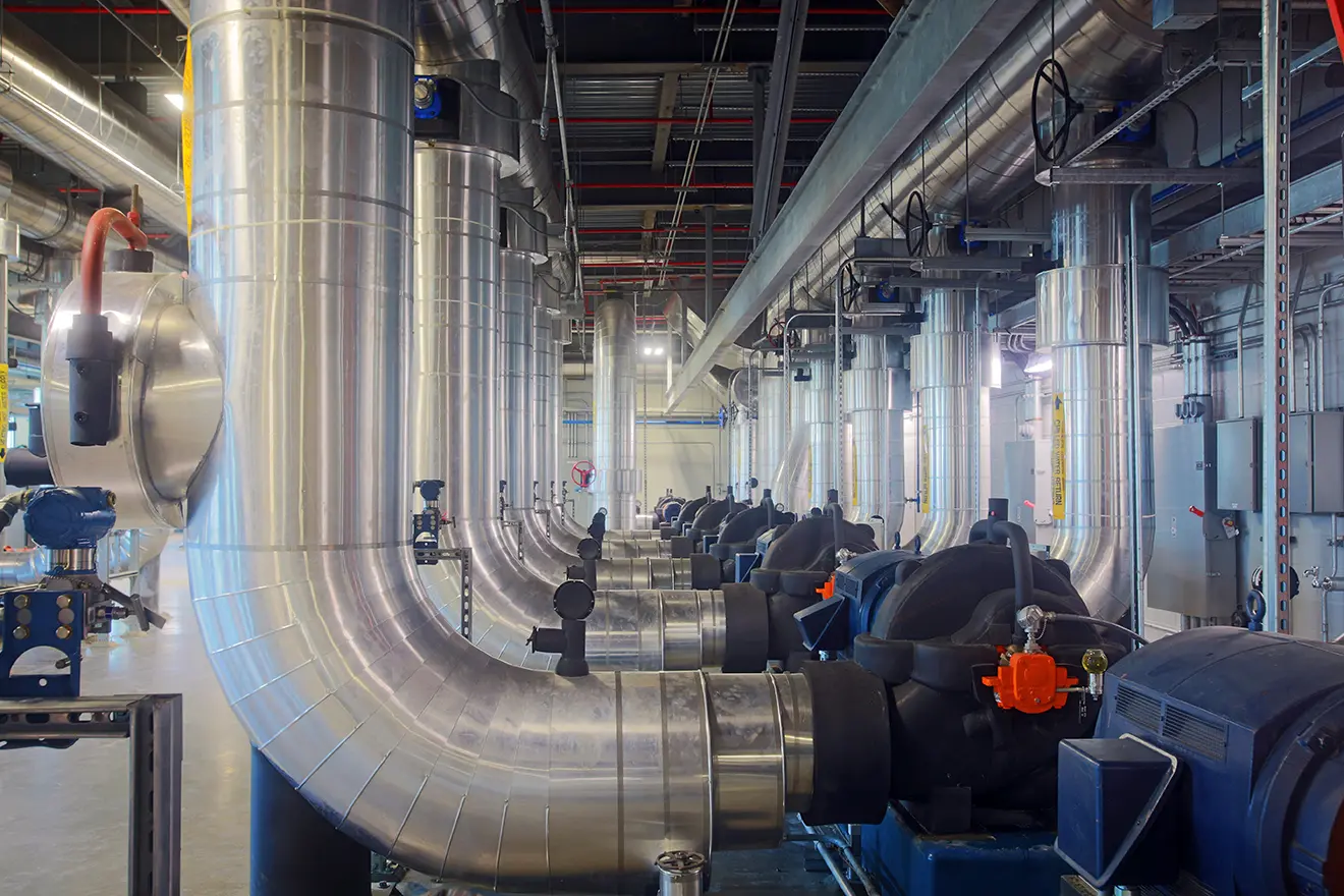A large industrial room filled with shiny metal pipes and machinery, arranged in neat rows. The setting is clean, bright, and organized.