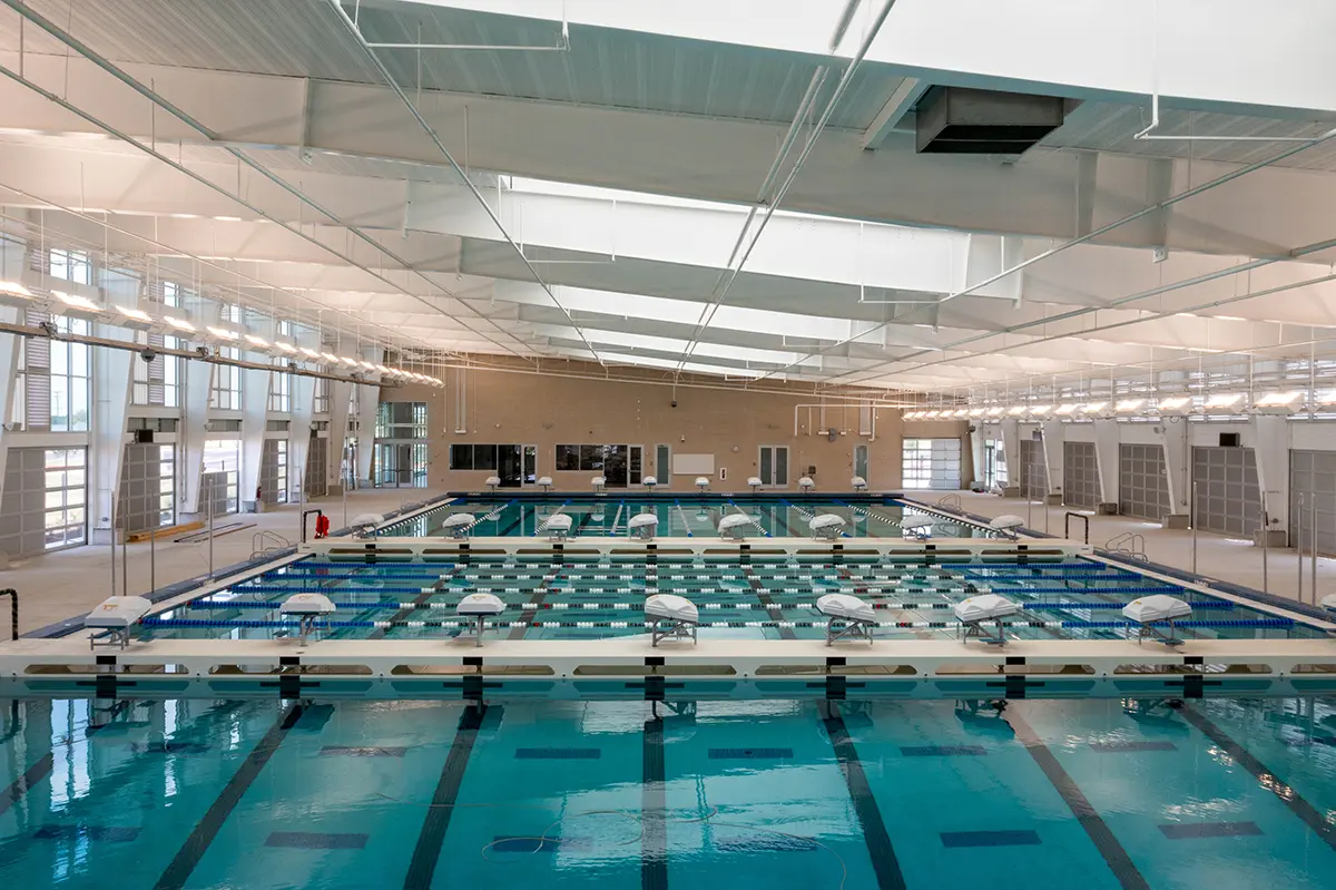 Spacious indoor swimming pool with multiple lanes, large skylights, and bright overhead lights. The atmosphere is clean, modern, and well-lit.