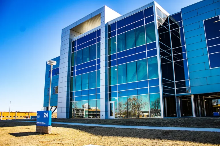 Modern glass office building on a clear day, with blue reflective windows surrounded by a grassy area.