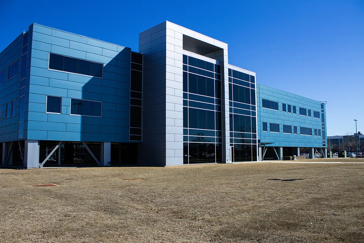 Modern blue and gray building with large windows, standing on a grassy field under a clear blue sky, conveying a sense of openness and innovation.