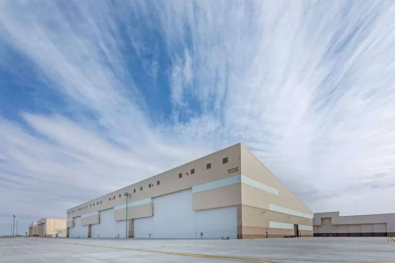 A large, beige warehouse set against a vast, expansive sky with scattered clouds.