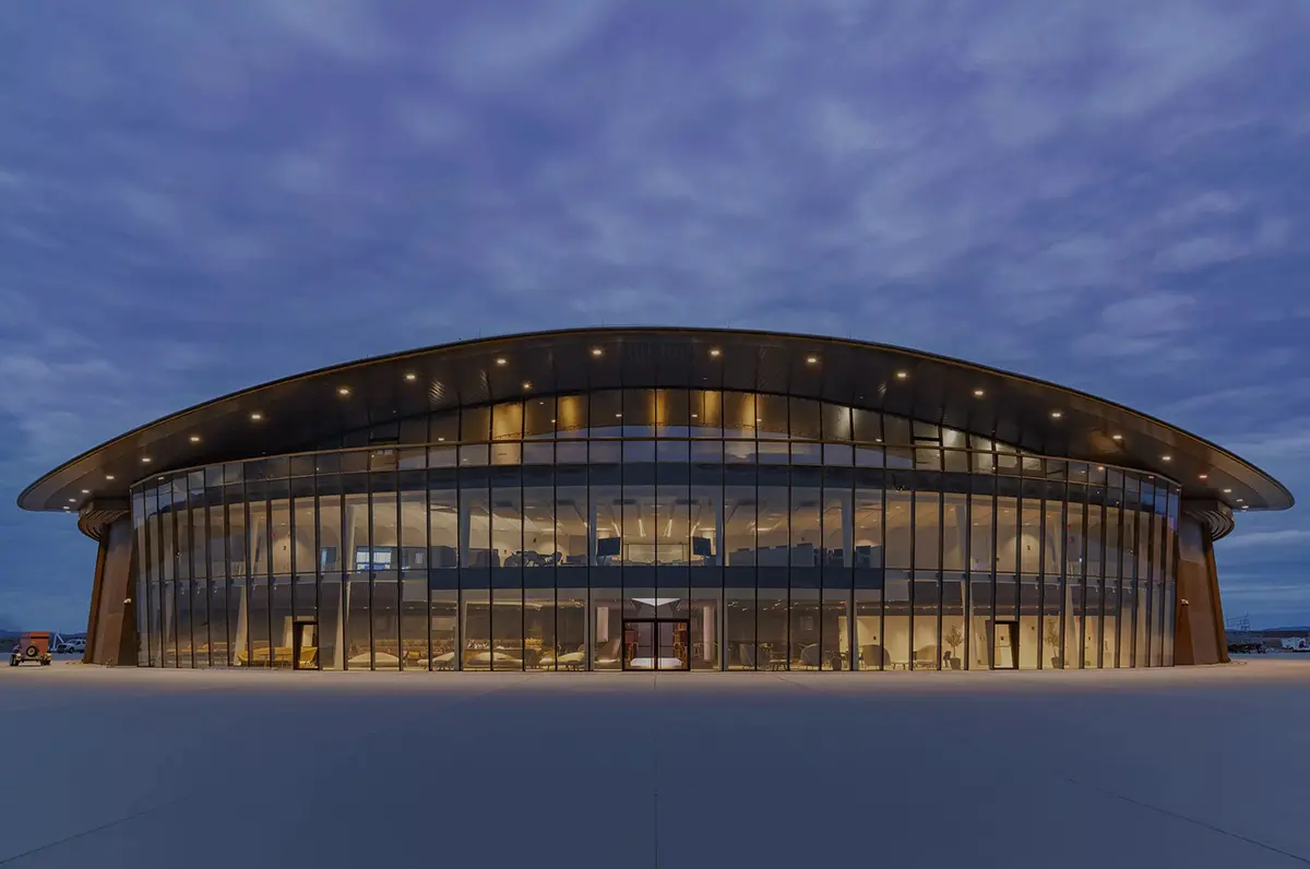 Modern building at twilight with curved, glass facade and glowing interior lights against a cloudy sky, conveying a futuristic and serene ambiance.