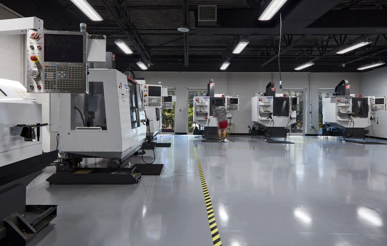 A modern factory floor with sleek, automated CNC machines aligned neatly. A person is operating one, creating a focused and industrious atmosphere.