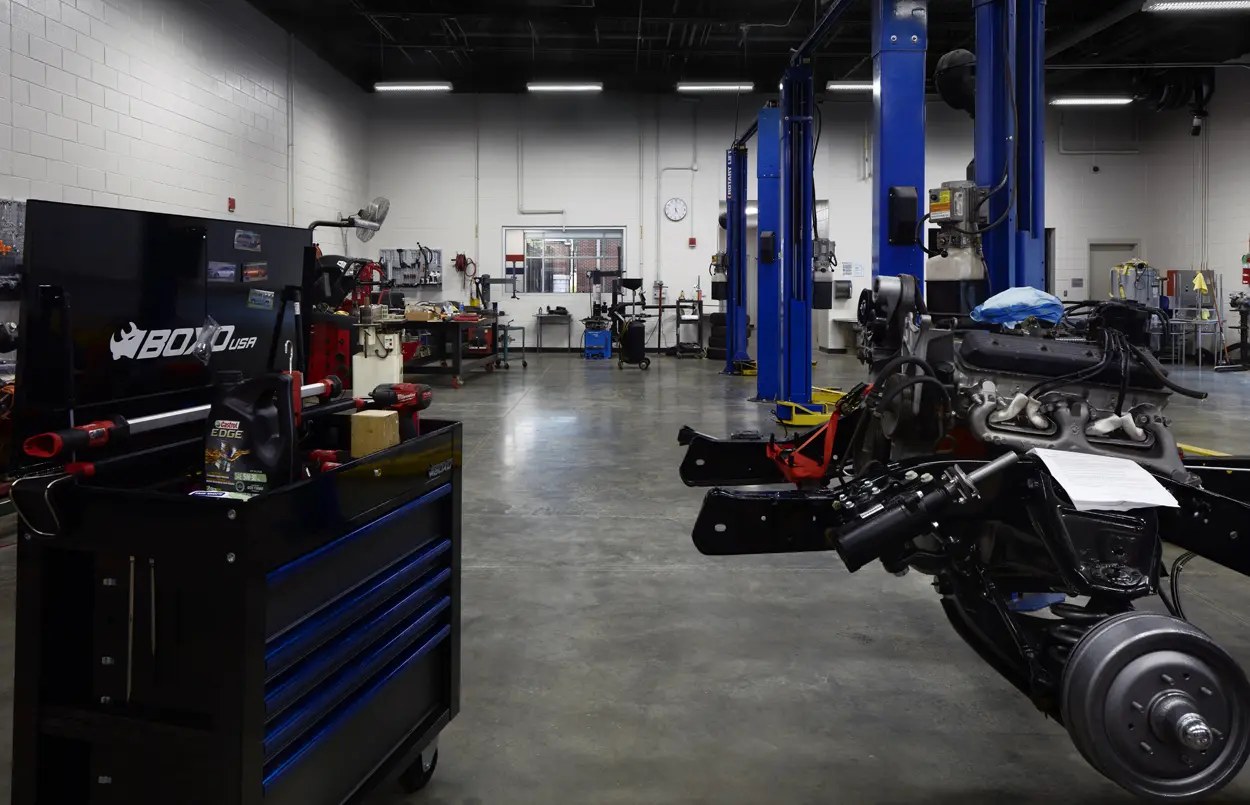 Spacious auto repair shop with blue lifts, a mounted engine, toolboxes, and assorted equipment. The atmosphere is organized and industrial.