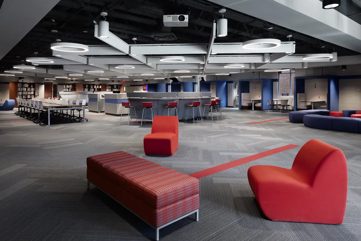 Modern lounge with red seating including chairs and a plaid bench, surrounded by circular lighting. Contemporary, open space with a relaxed vibe.