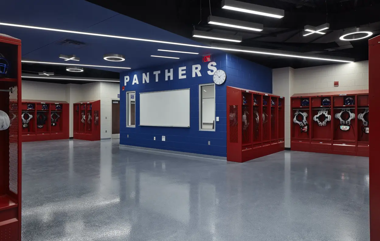 Modern locker room with blue walls and red lockers labeled "Panthers." Helmets and gear are neatly organized. Bright, clean, and orderly setting.