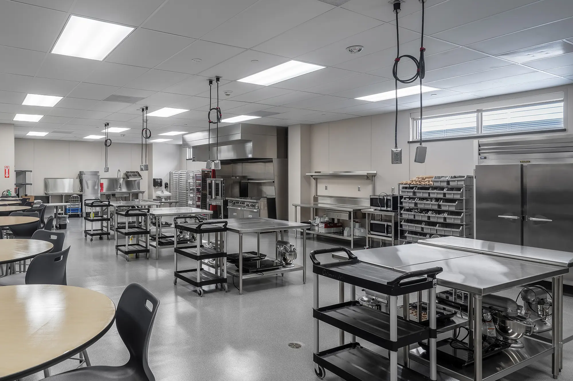 Commercial kitchen with stainless steel counters, ovens, and storage racks. The space is well-lit and organized, conveying a clean, professional atmosphere.