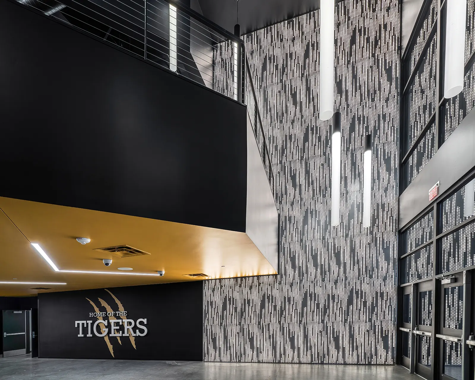 Modern interior with a high ceiling features a black wall with "Home of the Tigers" text and tiger claw marks. Vertical lights and a perforated pattern wall add contrast.