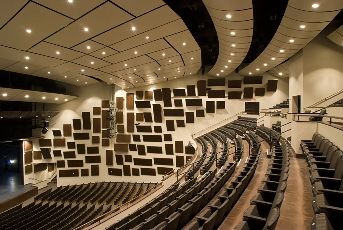 Modern auditorium with curved seating and geometric acoustic panels on the walls. The space is well-lit and conveys a sleek, professional atmosphere.