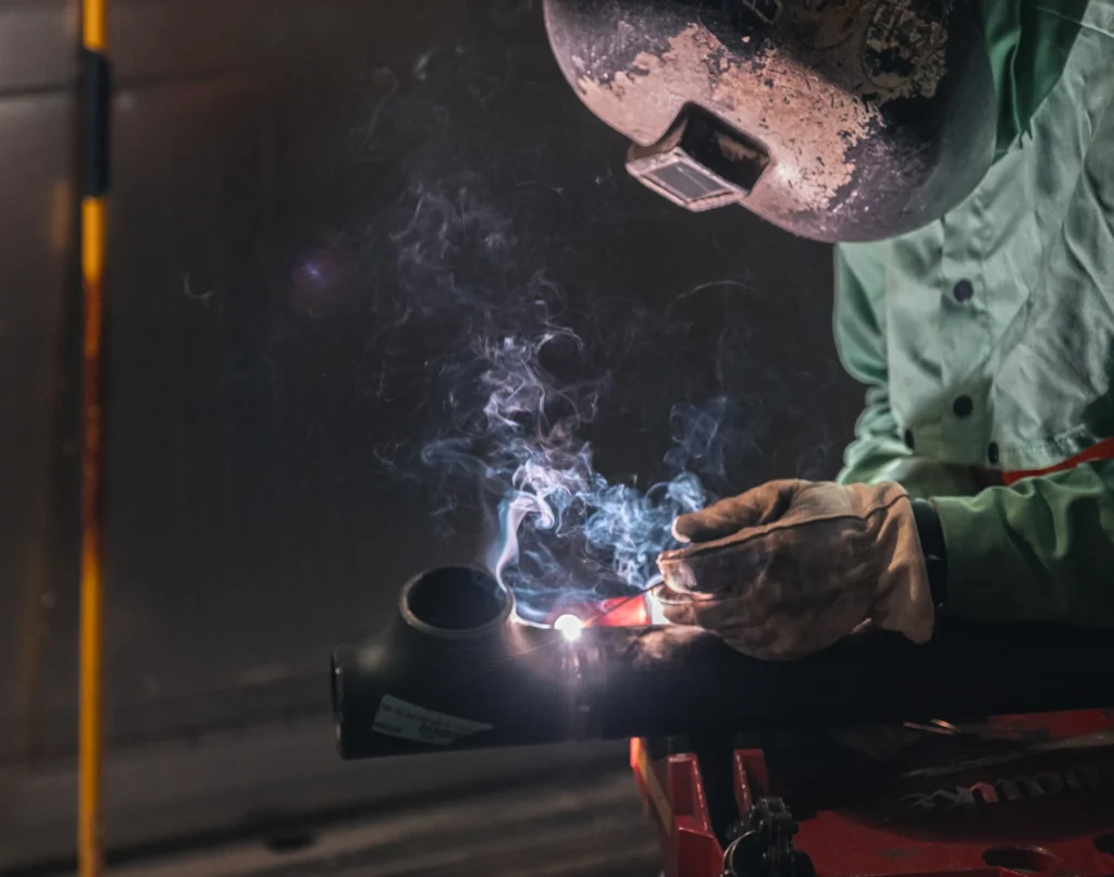 Three construction workers in orange vests converse at a building site. One holds a helmet. A sign reads "FLINTCO." The mood is professional and collaborative.