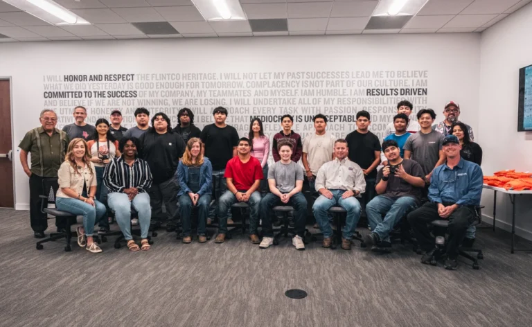 A diverse group of 20 people poses in an office setting, smiling and conveying a sense of teamwork and camaraderie. The background features motivational text on the wall.