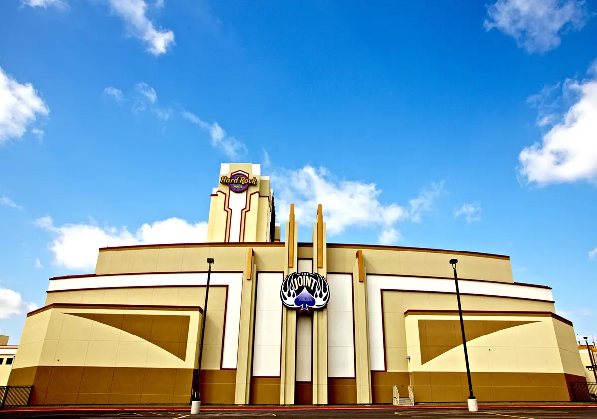 Art deco style building with vertical lines, featuring "The Joint" sign, against a vibrant blue sky. The tone is bold and dynamic.