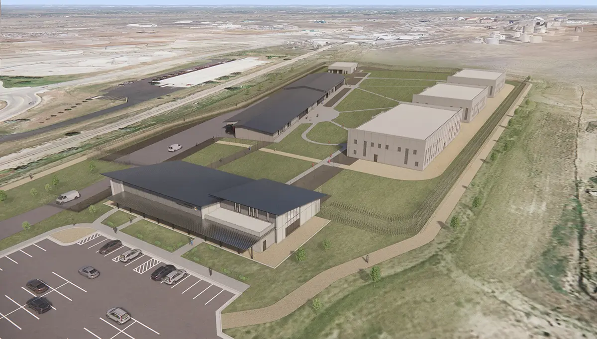 Aerial view of a modern industrial campus with multiple rectangular buildings, surrounded by grass and parking lot, set in a vast, open landscape.