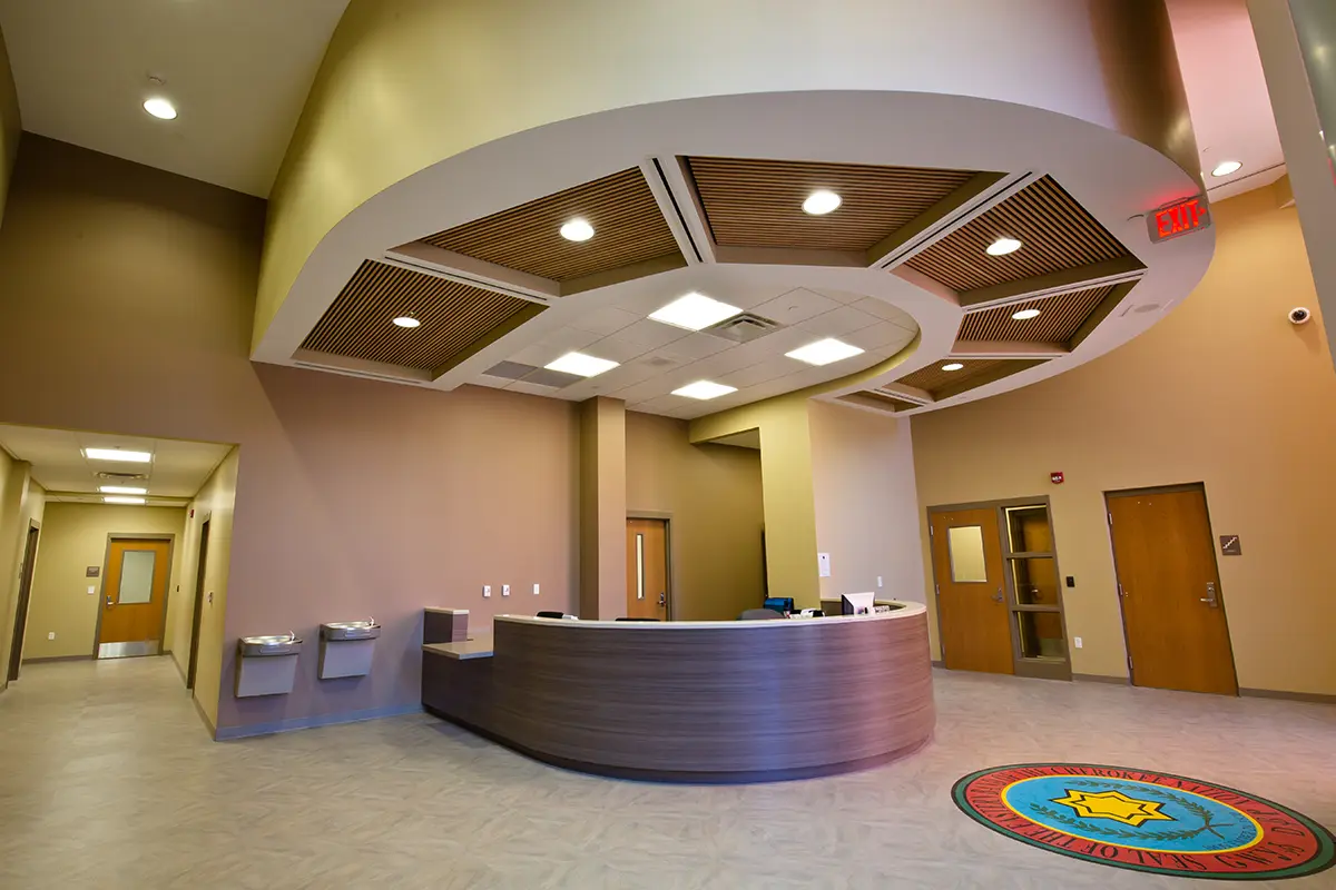 Spacious, modern reception area with a curved desk, overhead circular ceiling feature, and soft lighting. Hallways and doors extend in multiple directions.