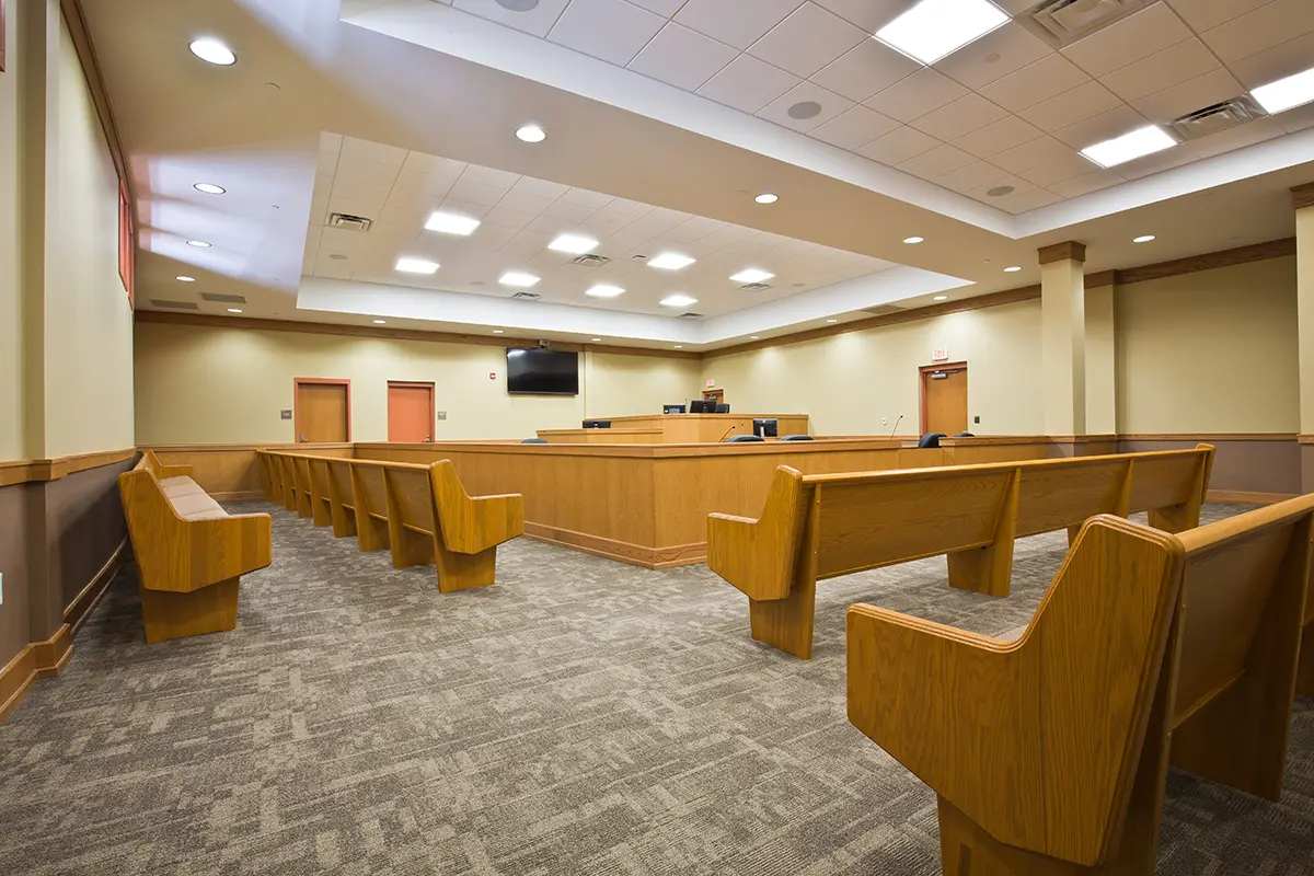 Empty courtroom with wooden benches and a judge's bench under bright ceiling lights. Neutral tones convey a formal, calm atmosphere.