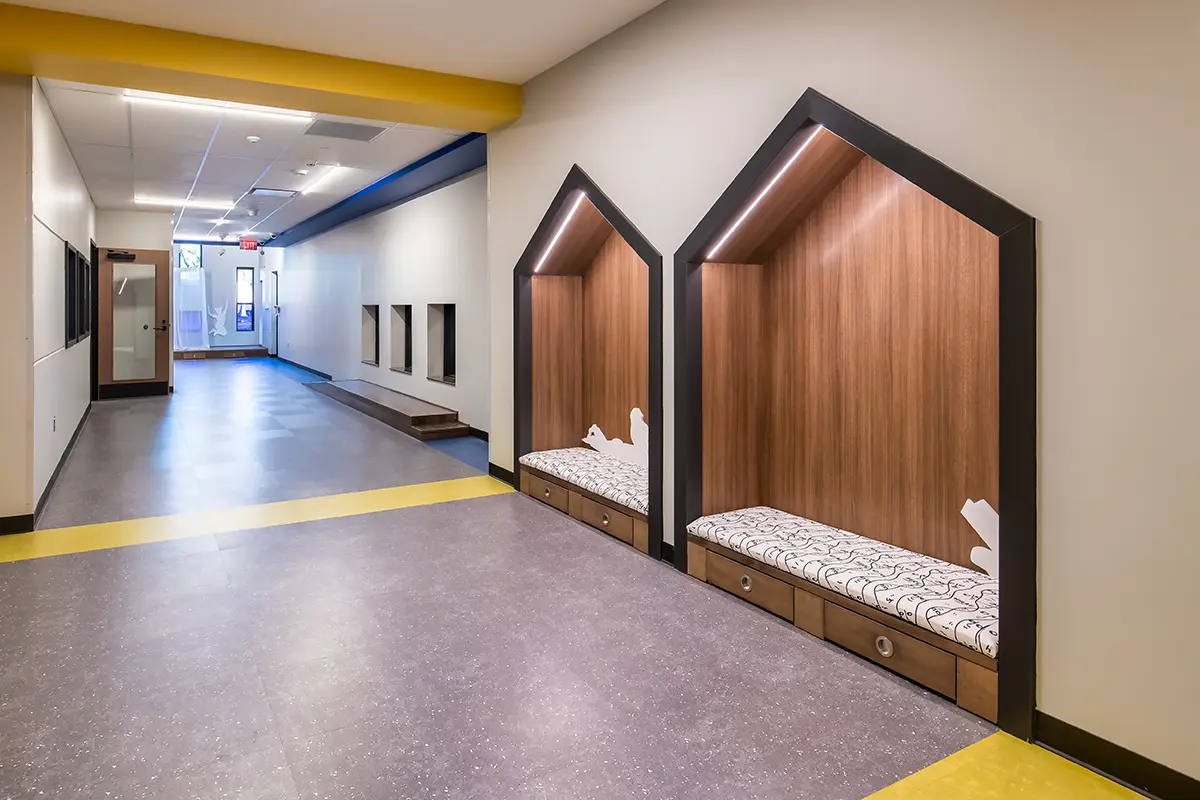 Modern school hallway with colorful flooring and unique wood-paneled seating alcoves shaped like small houses. Bright, inviting, and stylish design.