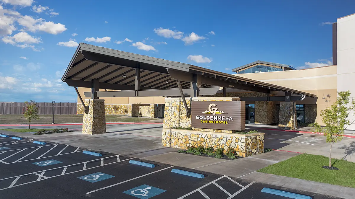 Modern hotel entrance with a wide canopy and stone accents under a clear blue sky. "Golden Mesa Casino Hotel" sign in front, accessible parking visible.