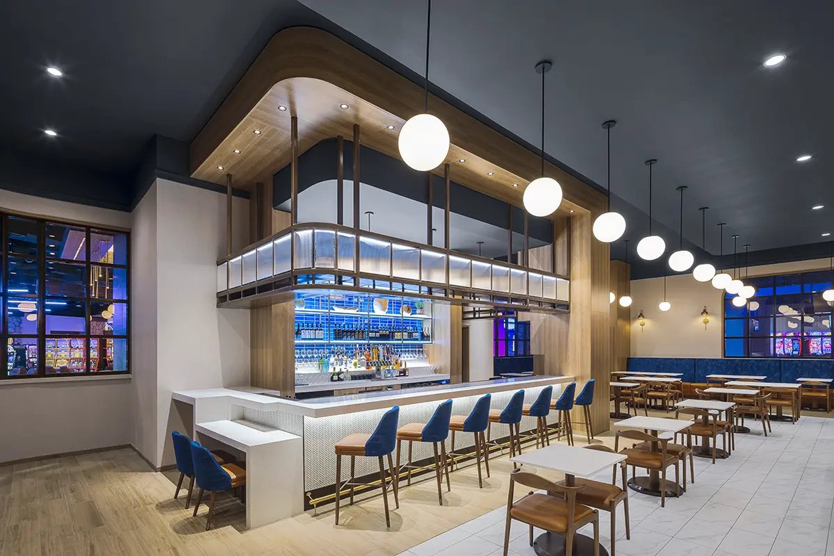 Modern hotel suite with a green and wood theme. Features a cozy seating area, a desk with a TV, and a bed framed by a large scenic artwork.