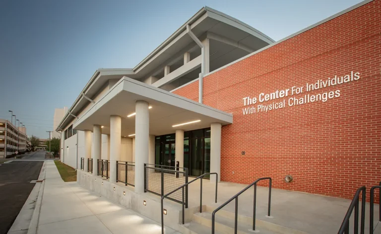 Modern building with a red brick facade, labeled "The Center for Individuals with Physical Challenges." Wide entrance ramp, welcoming and accessible.