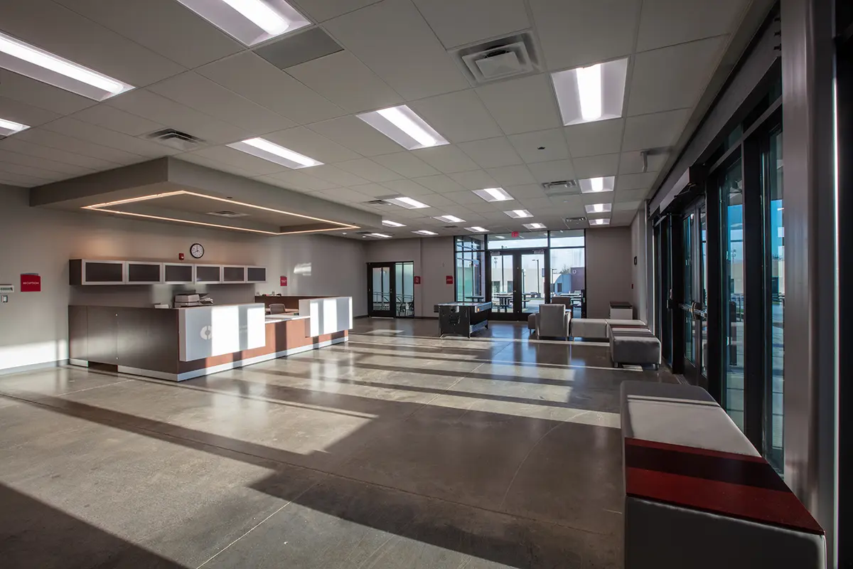 A spacious, well-lit lobby with modern decor. Features include a reception desk, large windows casting natural light, and seating areas, creating an inviting atmosphere.