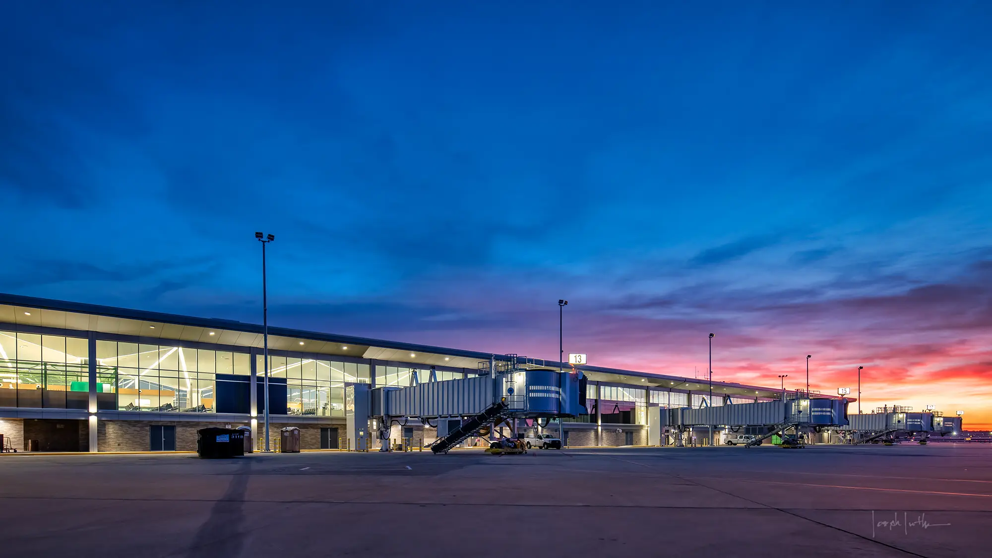 A modern airport terminal at dusk, with bright interior lights and a vivid blue and pink sunset sky, conveying a calm and organized atmosphere.