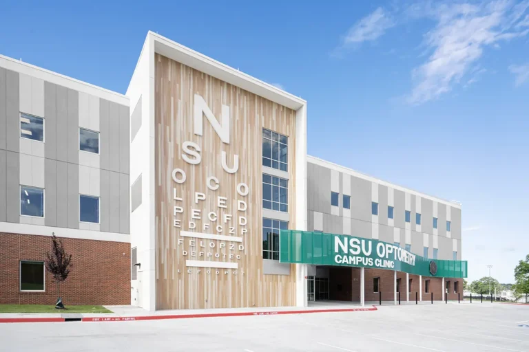 Modern clinic building under a blue sky with large eye chart letters on wood facade and "NSU Optometry Campus Clinic" in bold green on the glass canopy.