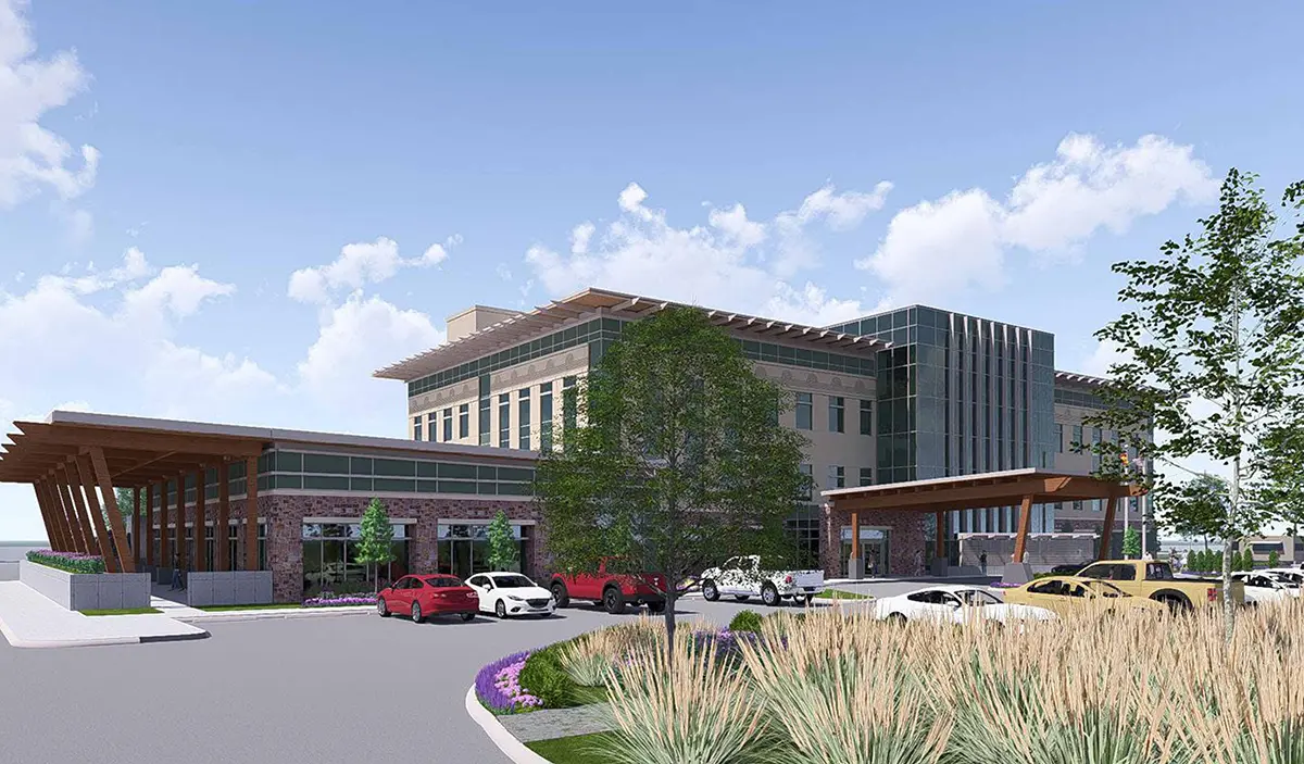 Modern building with large windows and wooden accents, surrounded by parked cars and greenery under a bright, partly cloudy sky. Calm, professional atmosphere.