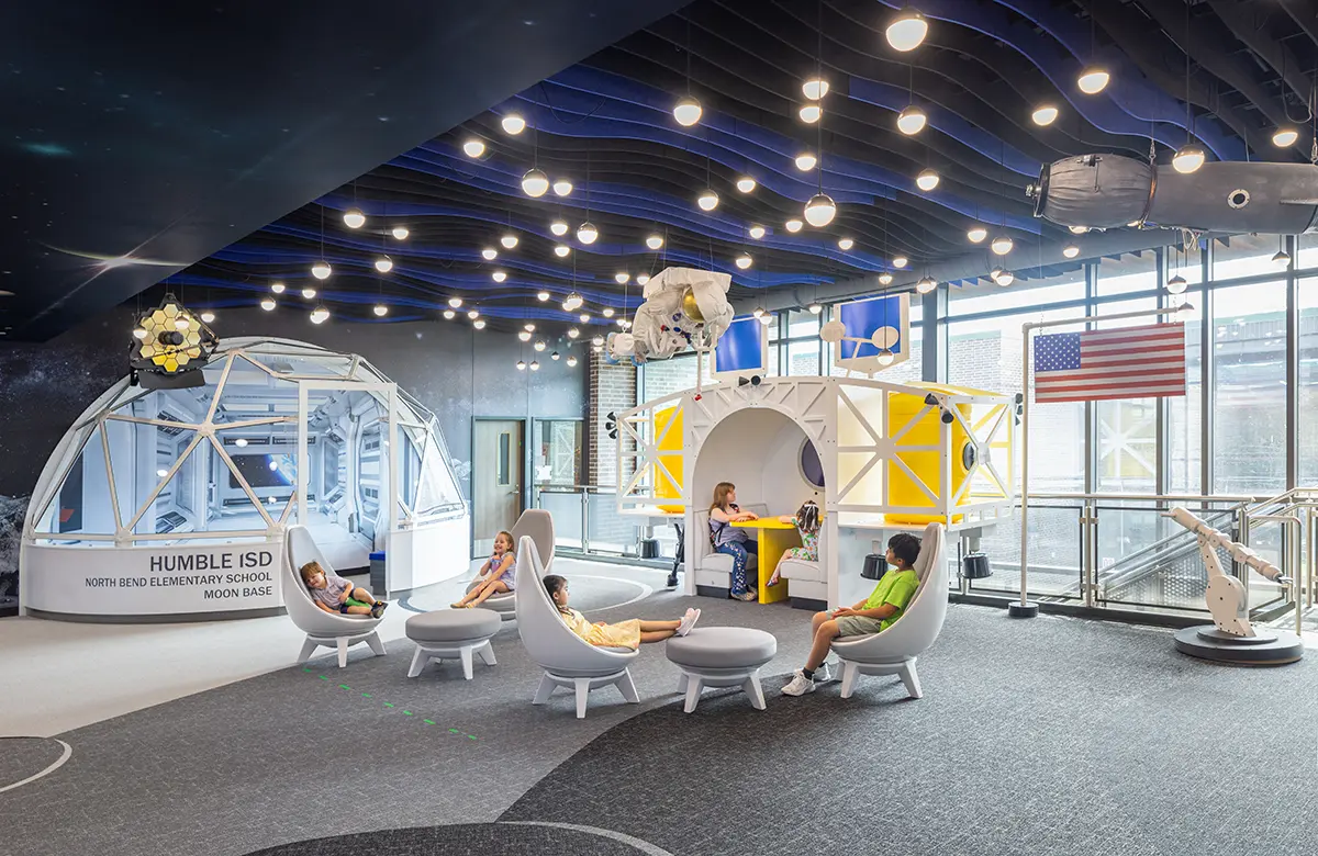 A futuristic classroom with a space theme, featuring modern chairs, a play structure resembling a moon base, and a ceiling with star-like lights. Kids are engaged and exploring.