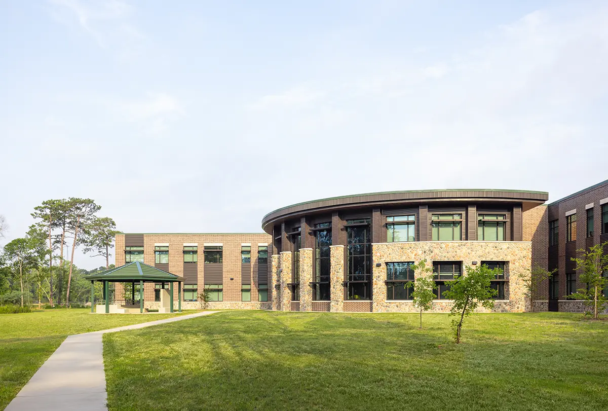 Modern building with a curved facade and large windows, set in a grassy area with a small gazebo and trees under a clear blue sky. Peaceful ambiance.
