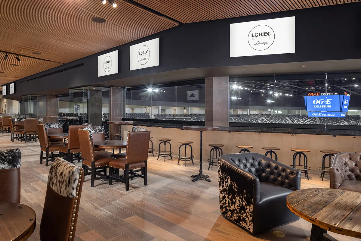 Luxurious lounge overlooking an arena, featuring cowhide and leather chairs, and rustic wooden tables. The atmosphere is upscale and inviting.