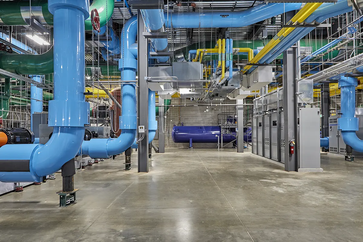 Interior of an industrial facility with large, colorful pipes in blue, yellow, and green. The spacious setting conveys a sense of modern industry.