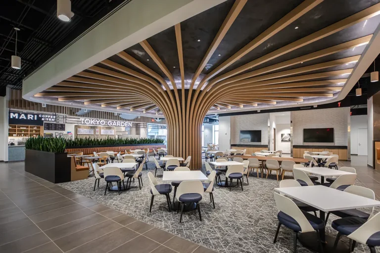 Spacious modern dining area with geometric ceiling beams, sleek tables, and chairs. Bright, airy atmosphere with "Tokyo Garden" and coffee shop signs.