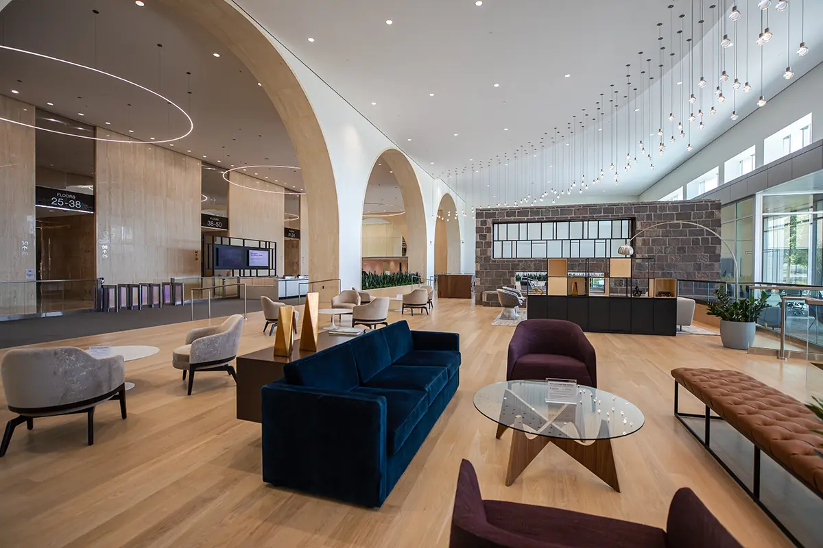 Amplio y moderno vestíbulo con techos altos y suelos de madera. Las paredes arqueadas, los elegantes sofás, las mesas redondas y las lámparas colgantes crean un ambiente acogedor.