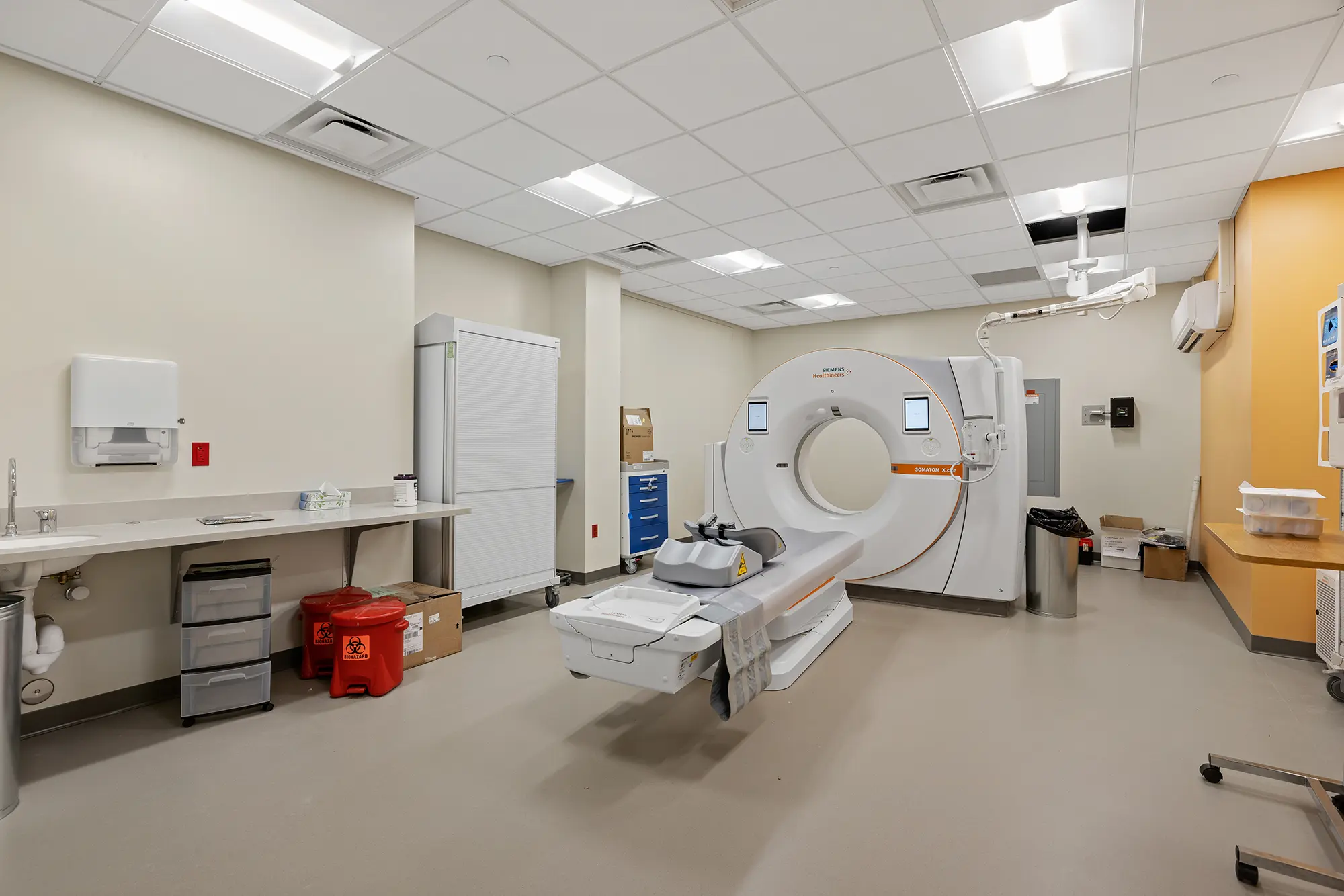 Modern hospital room with a CT scanner in the center. The room has white walls, a clean, organized appearance, and a calm, clinical atmosphere.